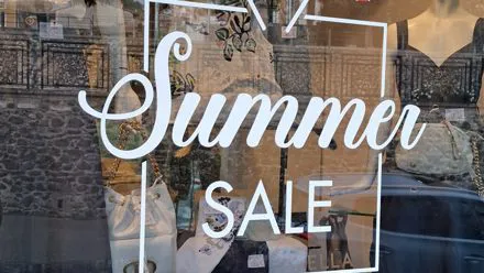 Vetrina con scritta adesiva Summer Sale e ombrelloni per la promozione dei saldi estivi