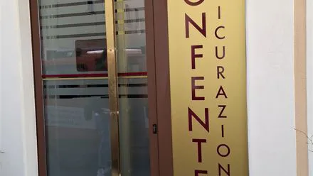 Porta a vetri di un'agenzia di assicurazioni con scritta adesiva dorata e logo HDI